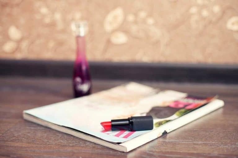 A red lipstick lying on a fashion book on a wooden desk.