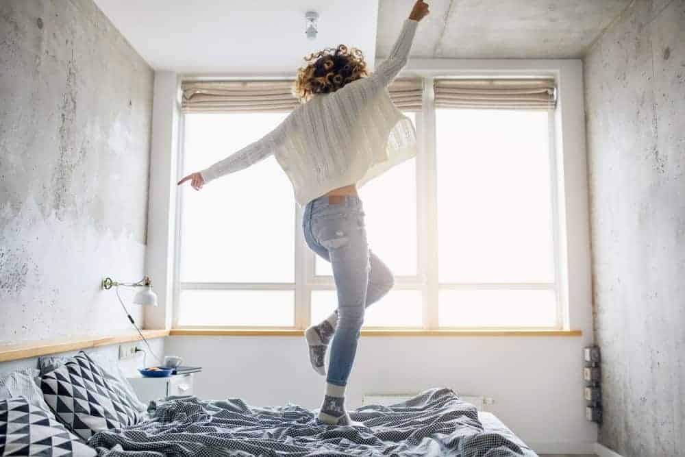 Femme en pull blanc sautant sur le lit.