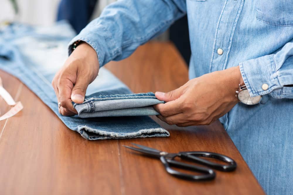 dette er et tæt kig på en skrædder, der arbejder på kanten af et par jeans.