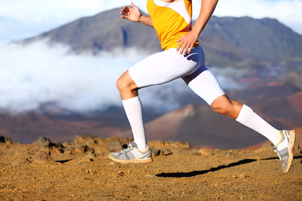 This is a close look at a man running on a mountain trail wearing a pair of compression shorts.