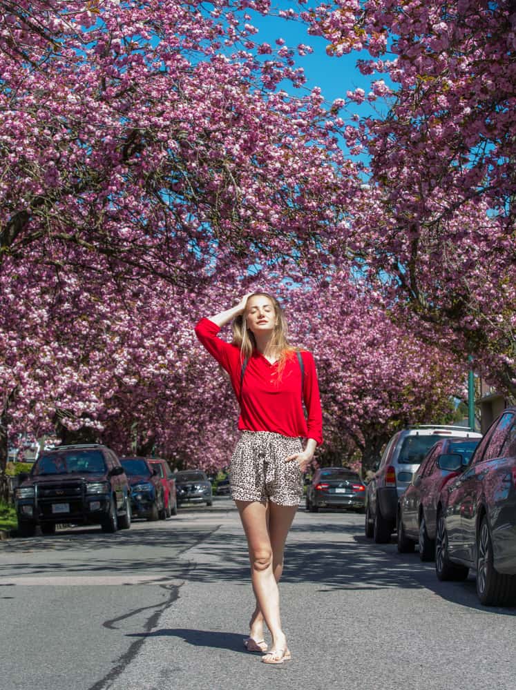 Une femme portant un short marche dans une rue bordée d'arbres à fleurs roses.