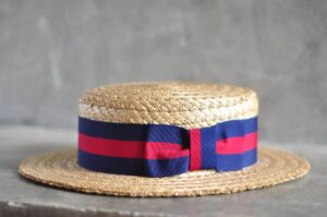 Single straw boater hat with red and blue hat band wrapped around crown against grey background