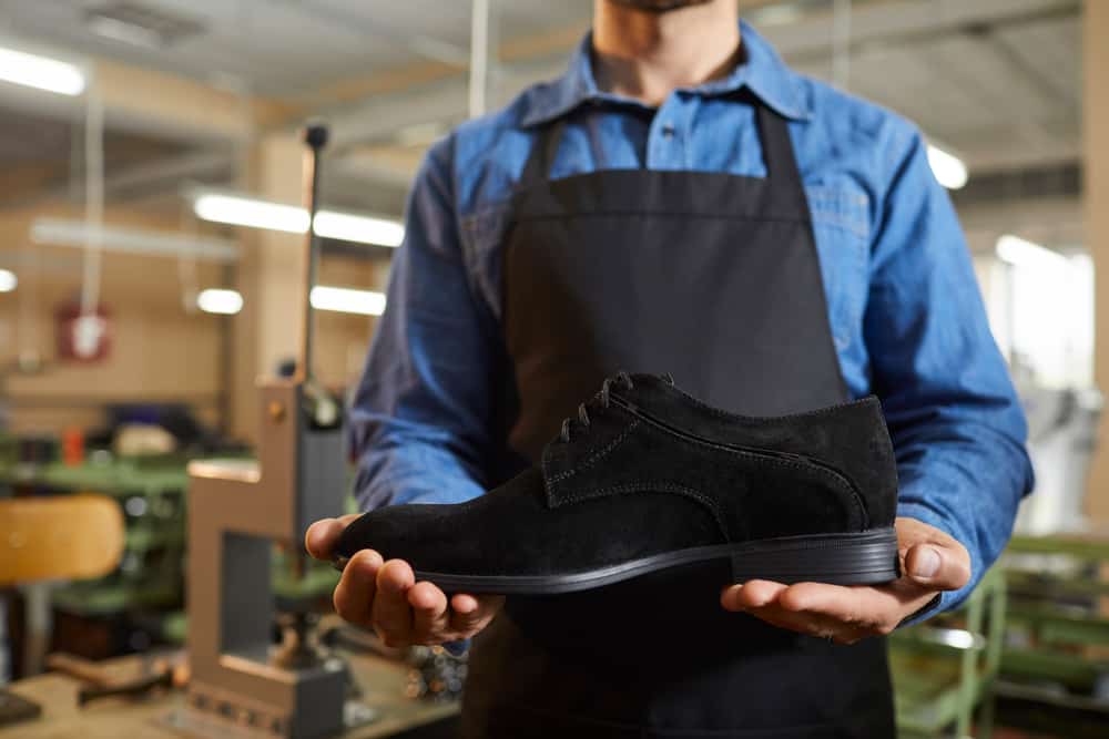 A shoemaker holding a finished black suede shoe.