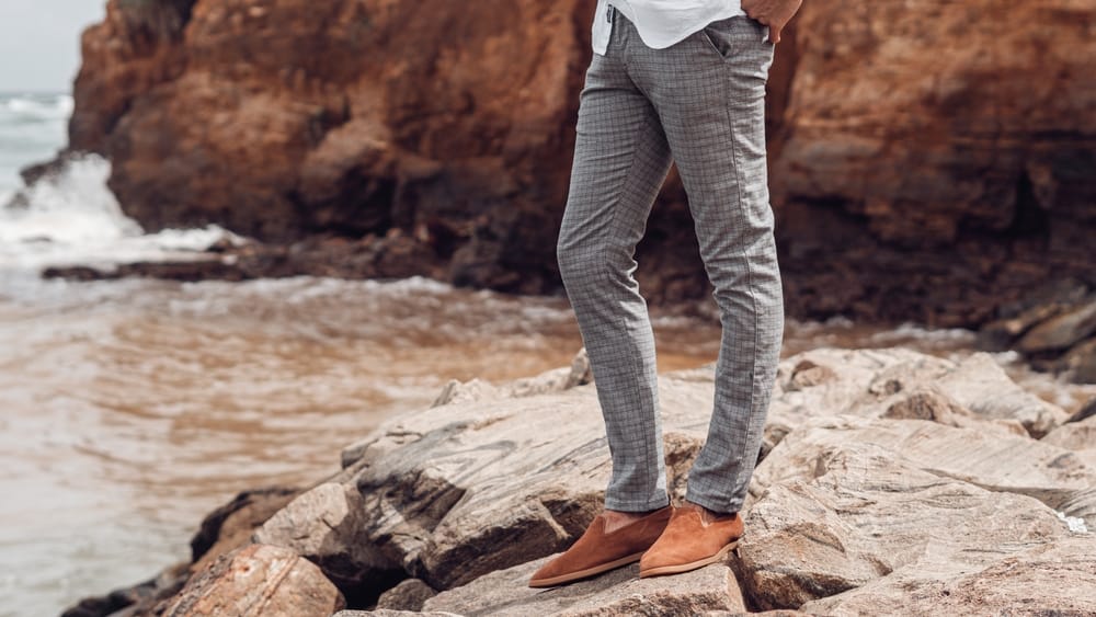 Man in chinos and brown loafers poses near the beach.