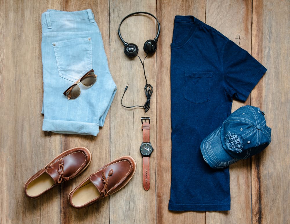 Men's outfit including a henley shirt, denim shorts, and loafers against a wooden background.