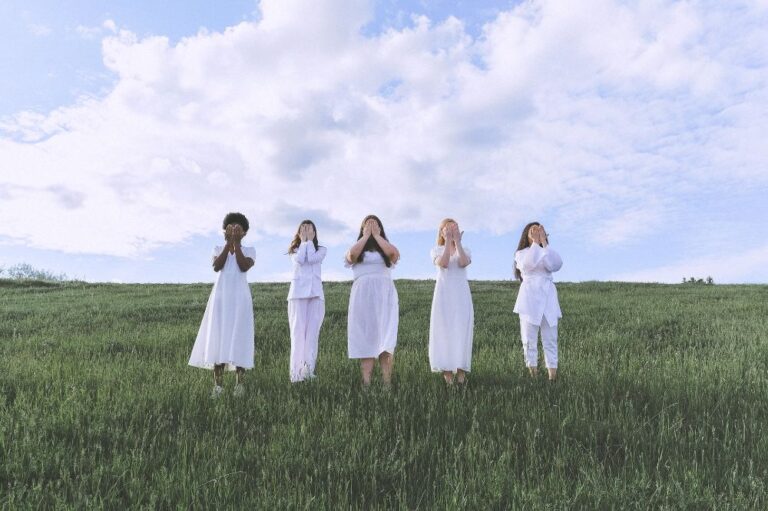 Women wearing white dresses standing in a grassy field