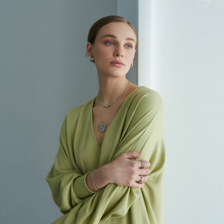 Person wearing a light green top and silver jewelry, standing indoors with arms crossed.