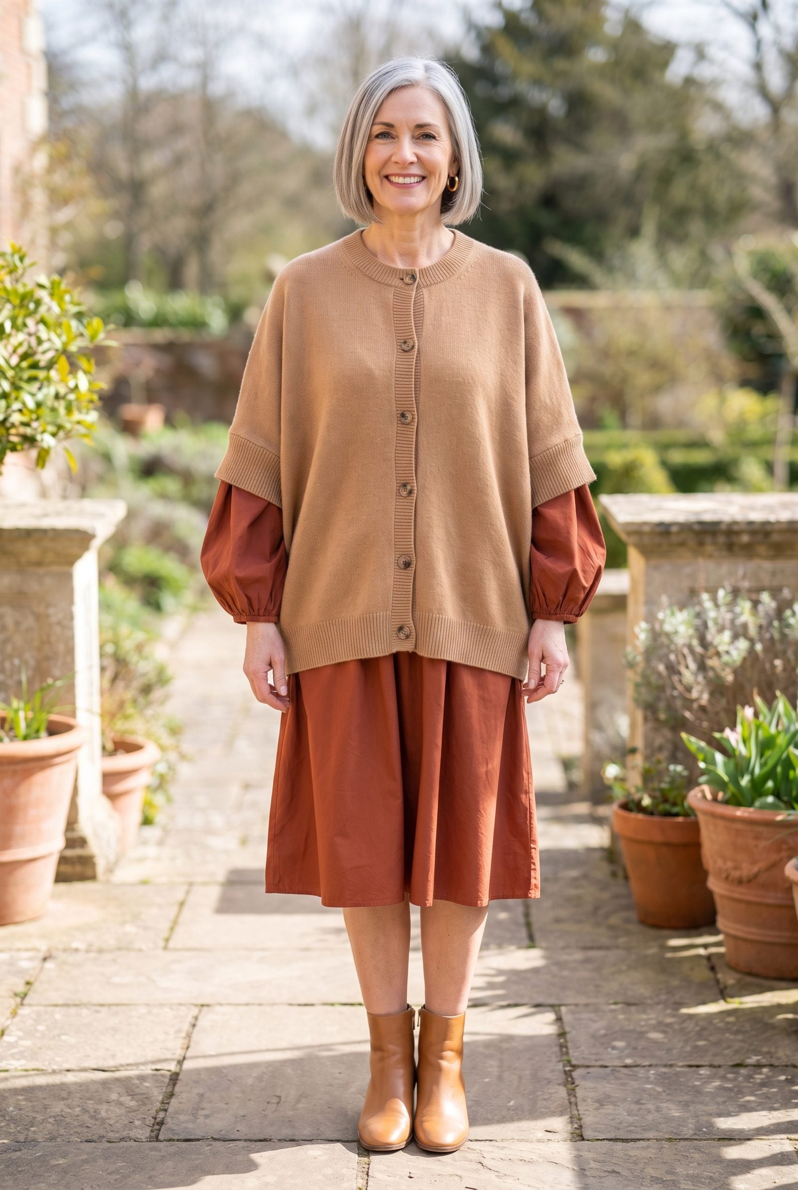 Woman in a rust puff-sleeve dress under a camel batwing cardigan whose wide sleeves stack over the dress sleeves and add