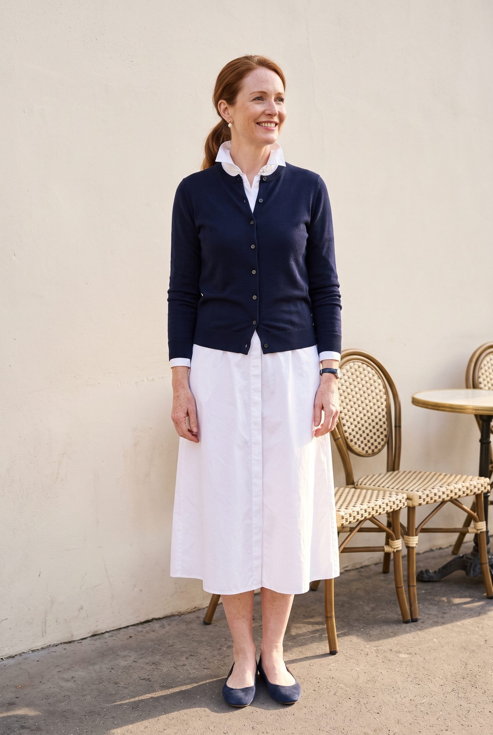 Woman in a white collared shirtdress under a navy cardigan buttoned to the throat, the collar crushed underneath.