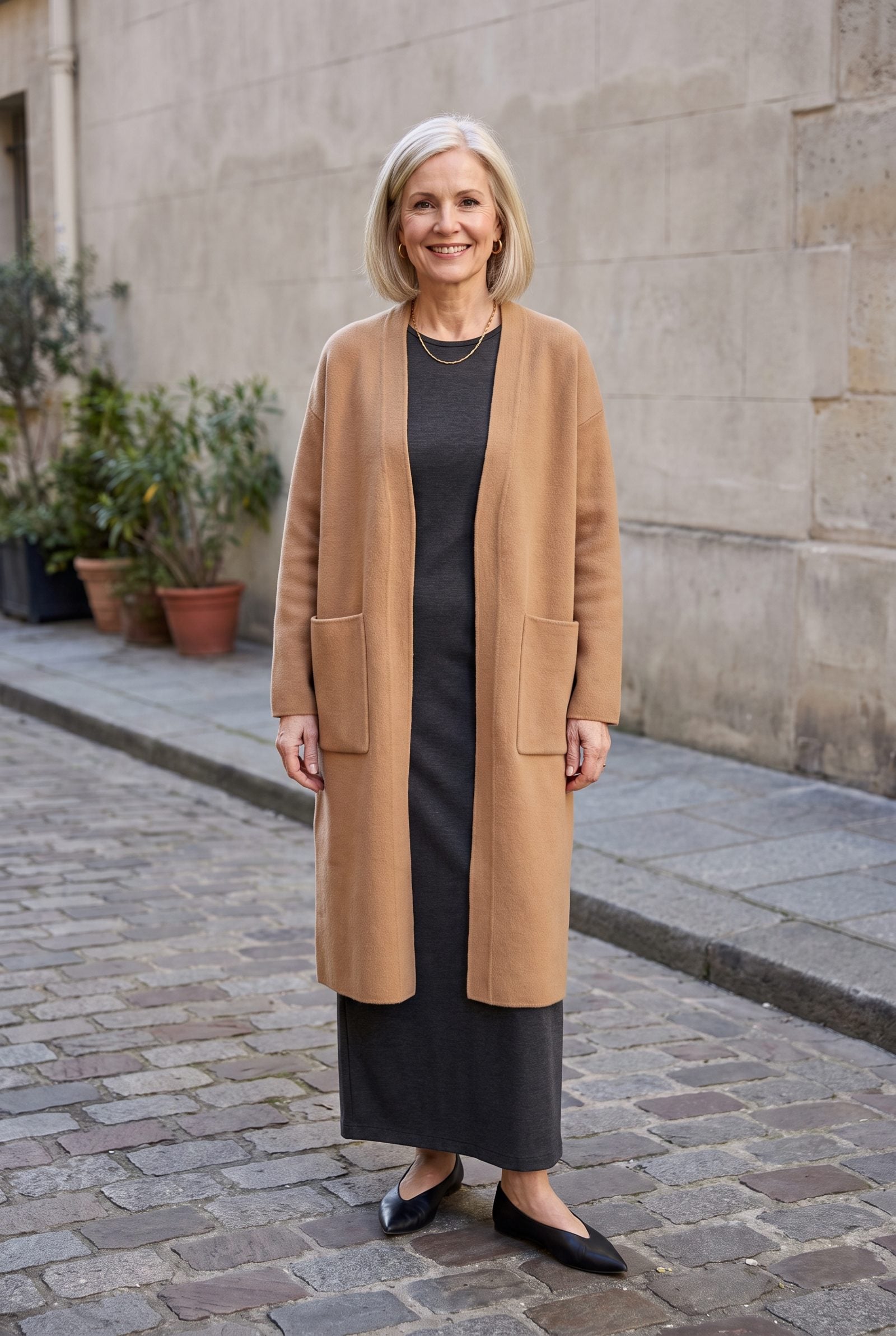 Woman in a charcoal column dress under a camel cardigan with two ten-inch patch pockets at hip level.