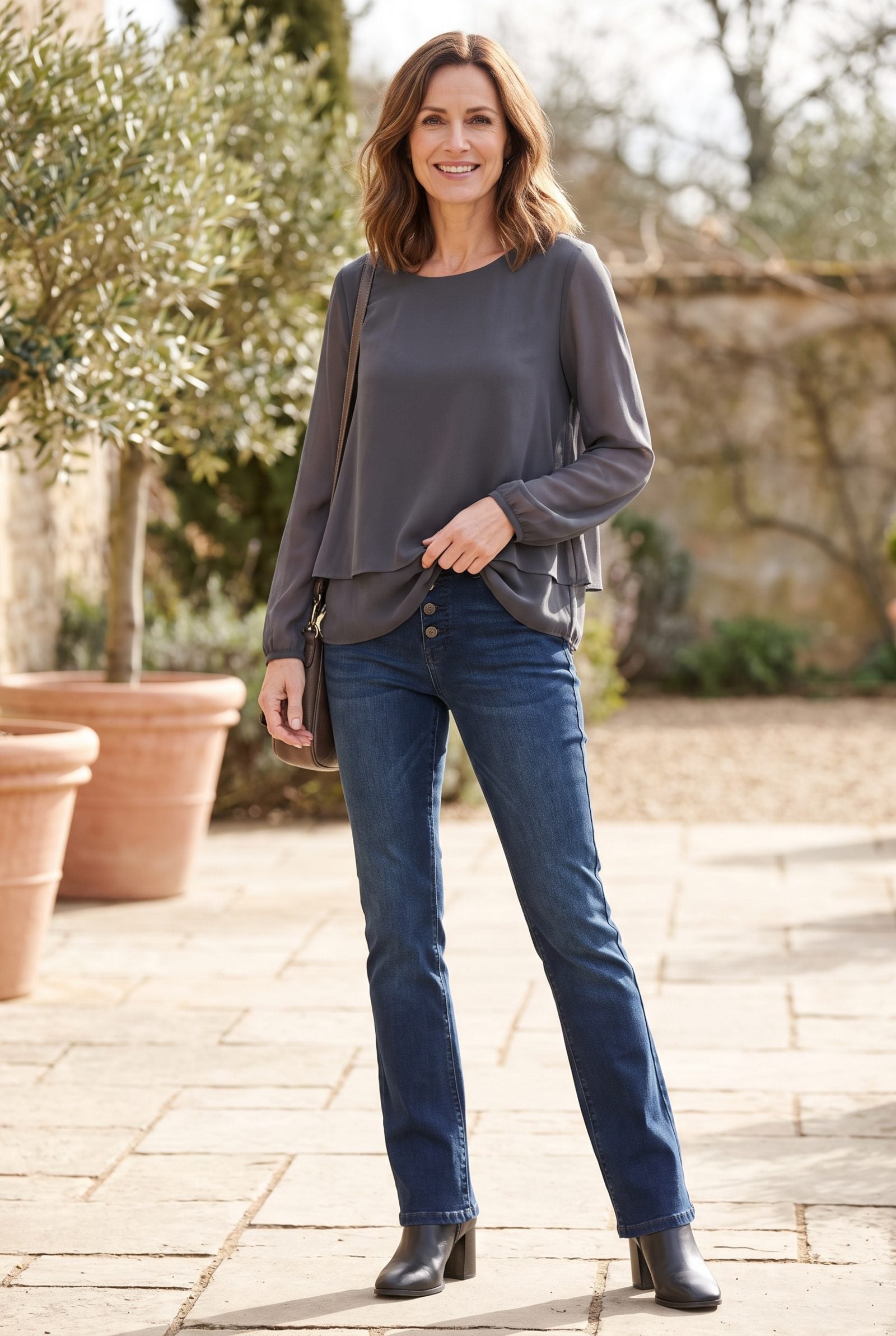 Woman in a cream double-layered blouse tucked into slim bootcut jeans, both layers bunching and thickening the waistband.