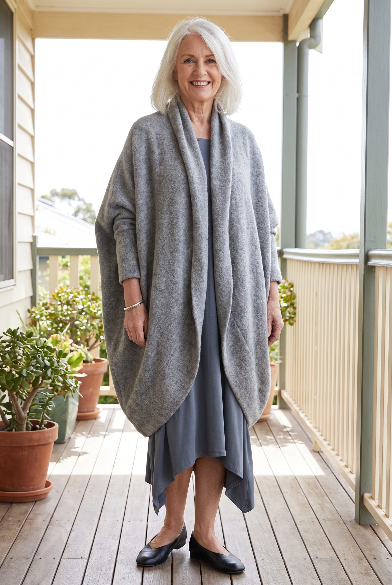 Woman in a slate asymmetric-hem dress under a dove grey cocoon cardigan whose curved hem covers and obscures the dress's