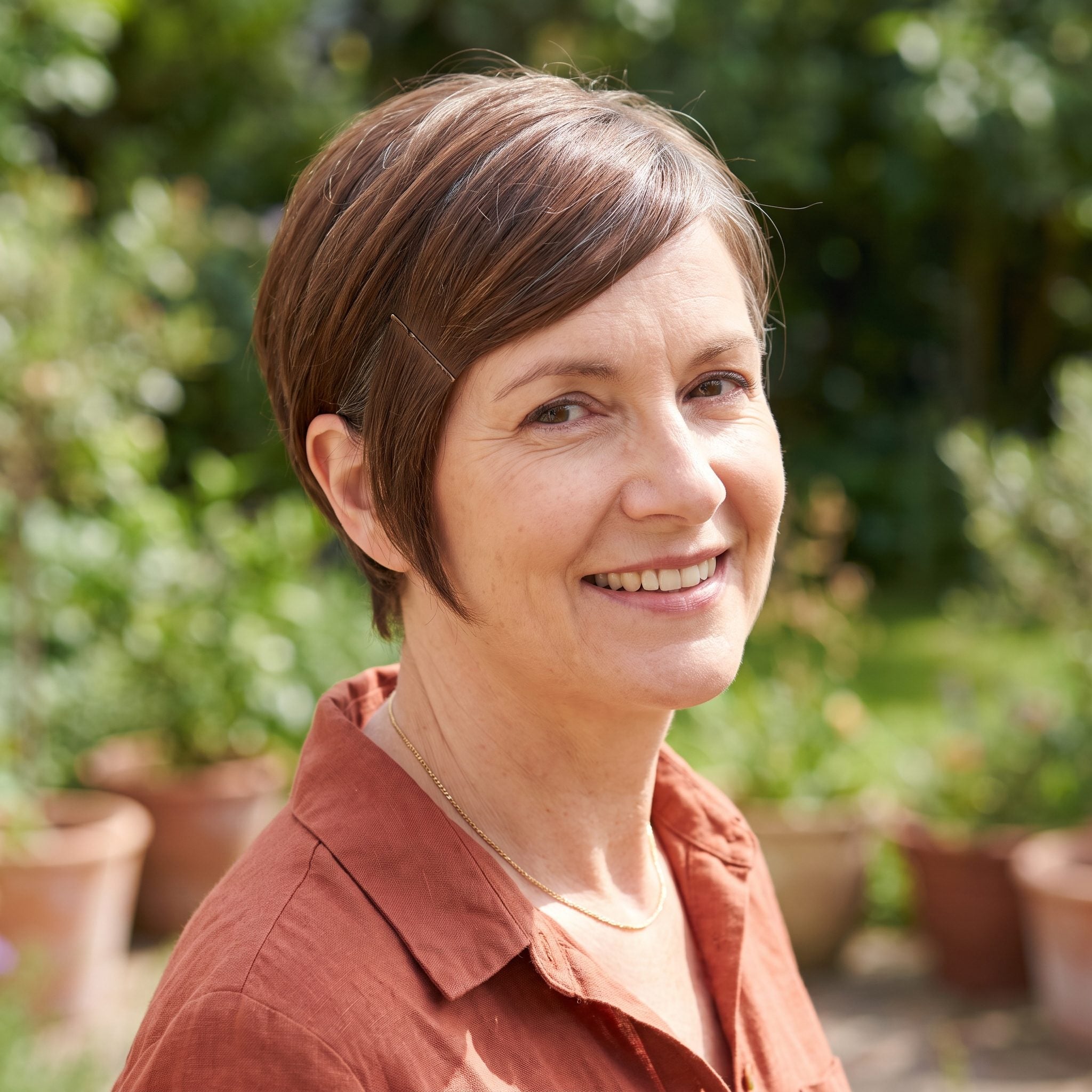 Woman with a chestnut pixie and long fringe pinned flat against one temple