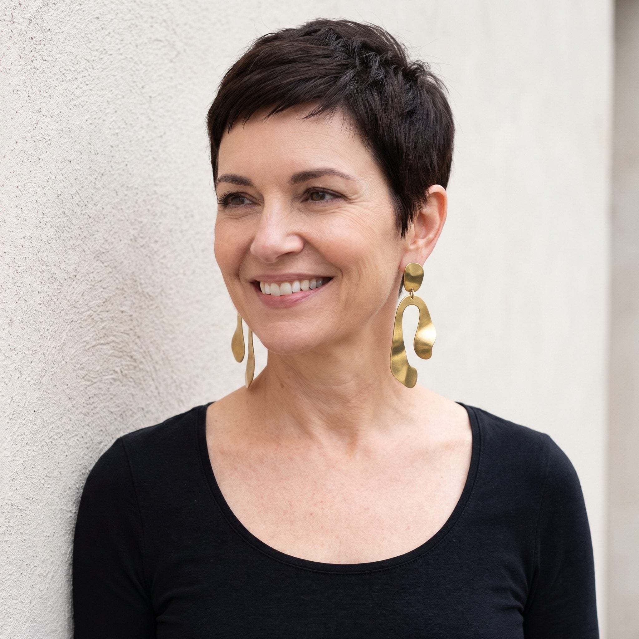 Woman with a sharp espresso pixie wearing oversized brass drop earrings