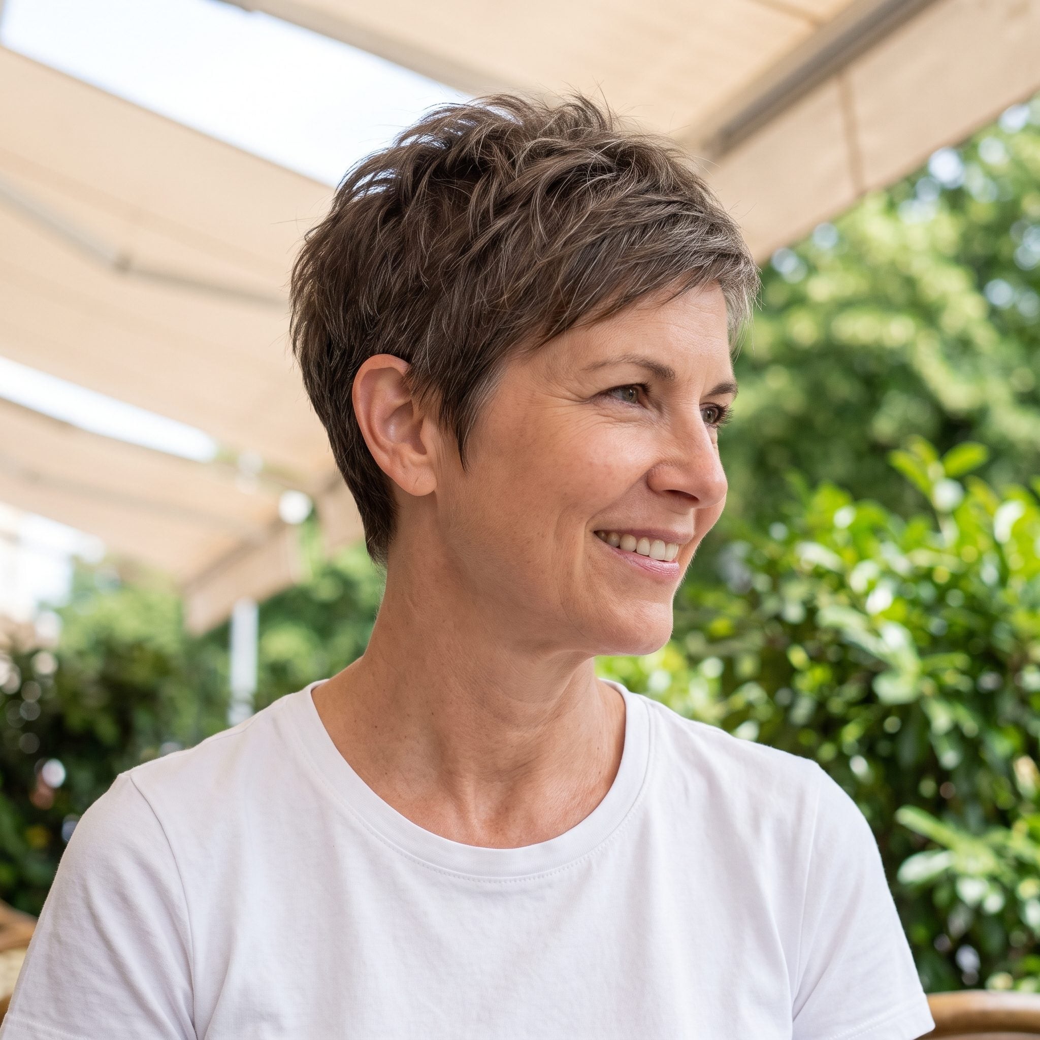 Woman with a soft textured brown-gray pixie and a completely bare neckline and ears