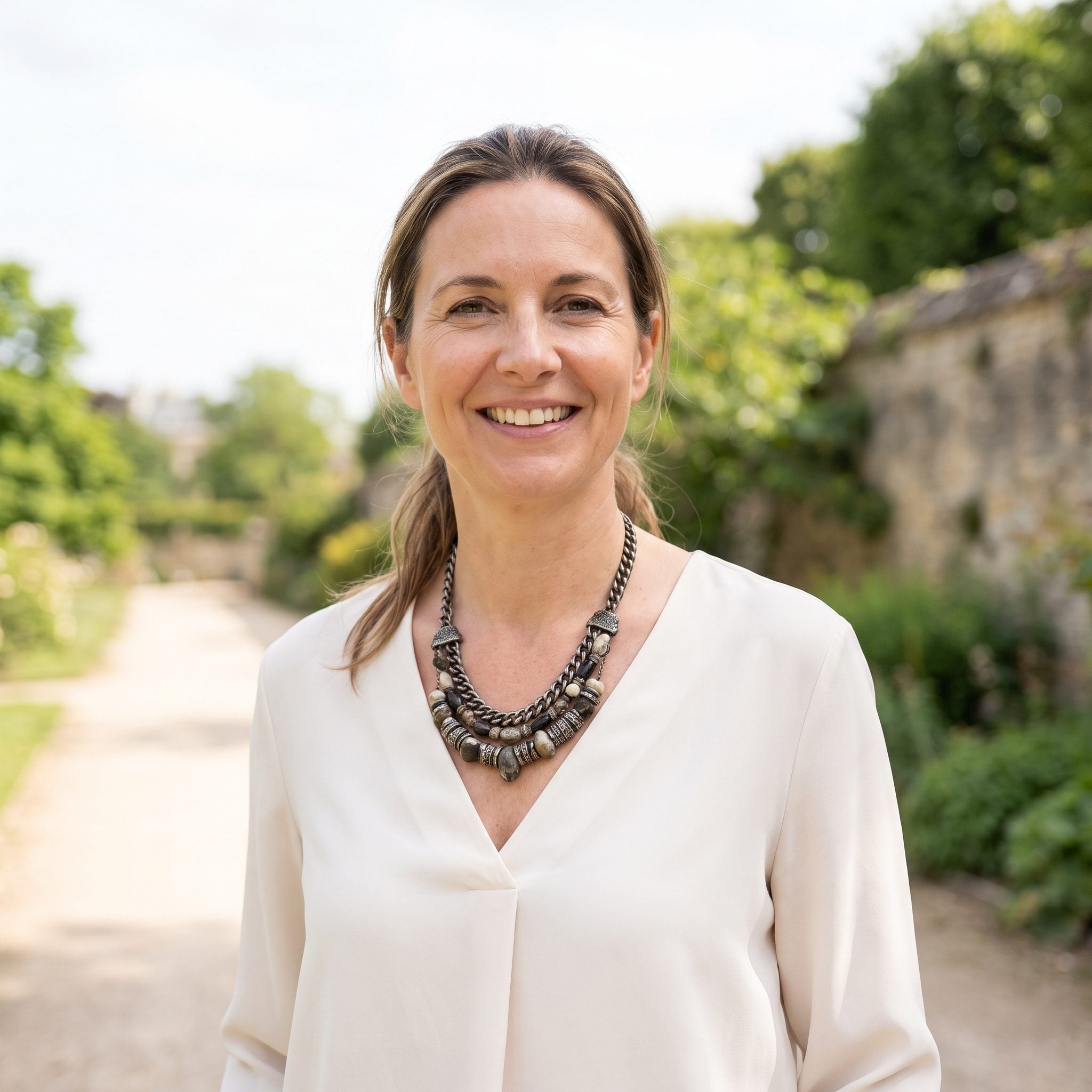 Woman in a cream V-neck blouse with a statement necklace resting exactly across the point of the V.