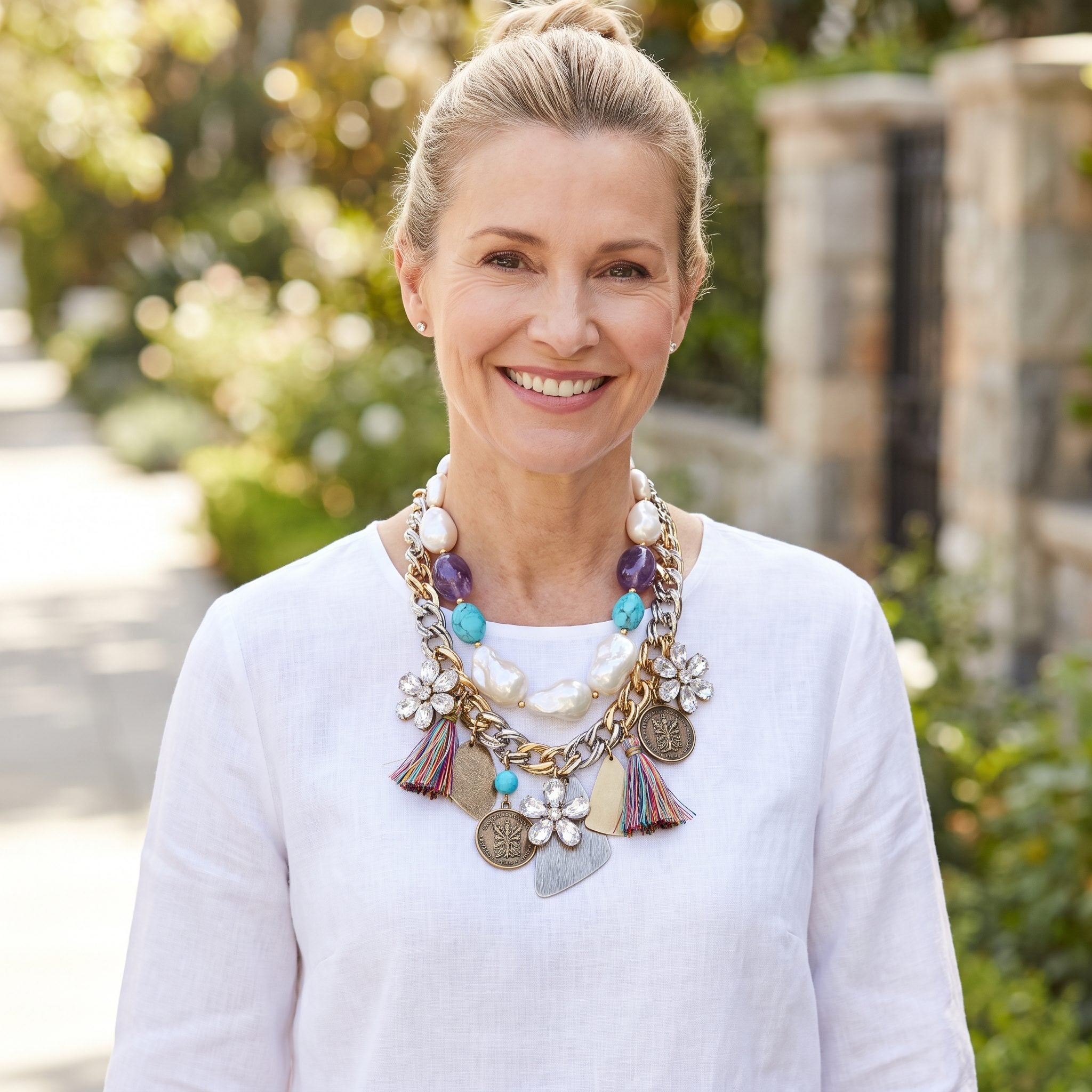 Woman in a plain white blouse wearing a single necklace combining pearls, gems, chains, tassels and medallions.