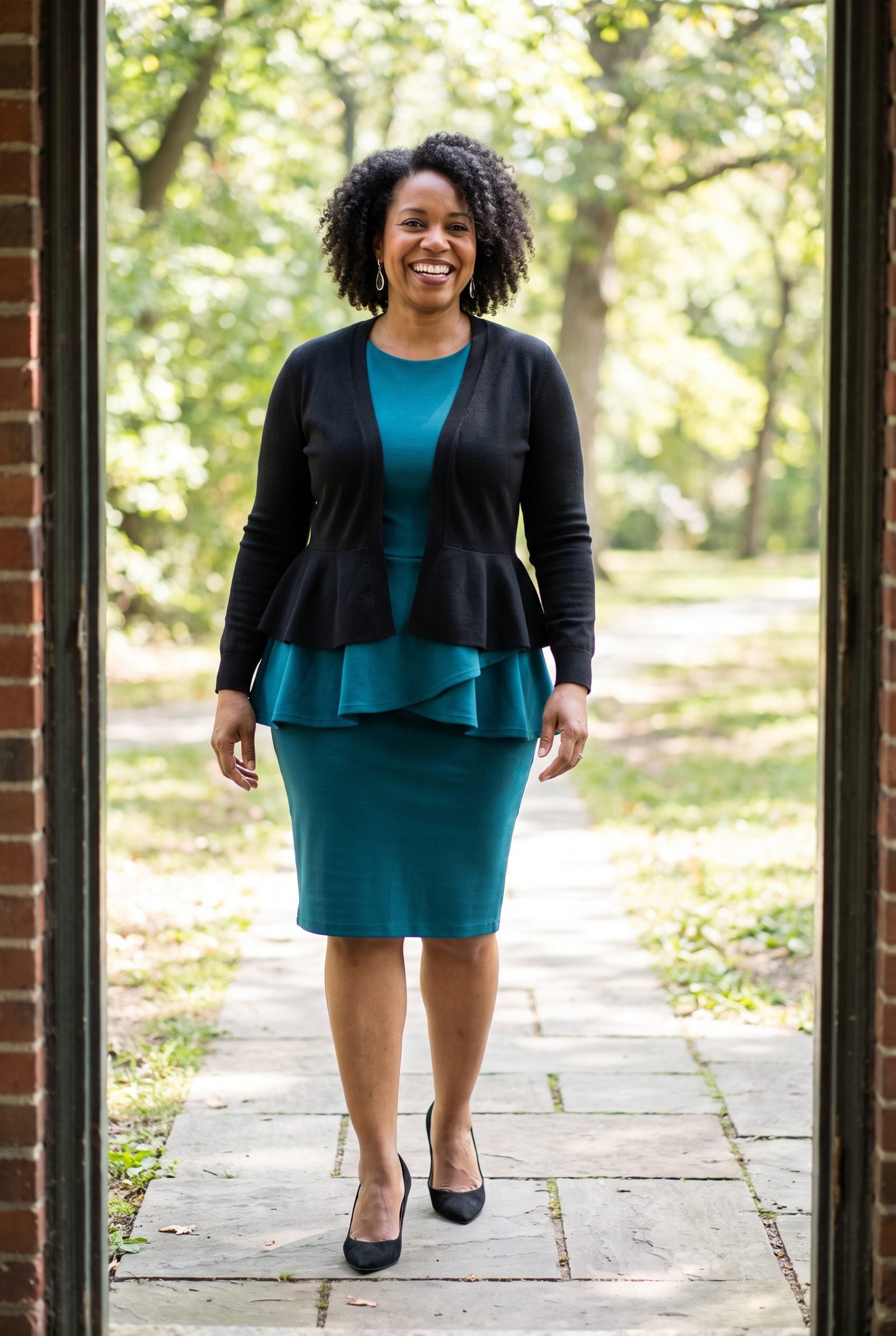 Woman in a teal peplum dress under a black peplum cardigan, two peplum flares stacked at the waist.