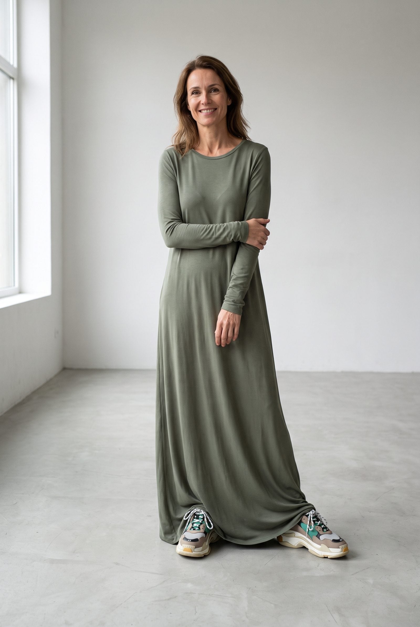 Woman in a grey jersey maxi dress with bulky dad sneakers, the hem pooling about three inches on the ground.