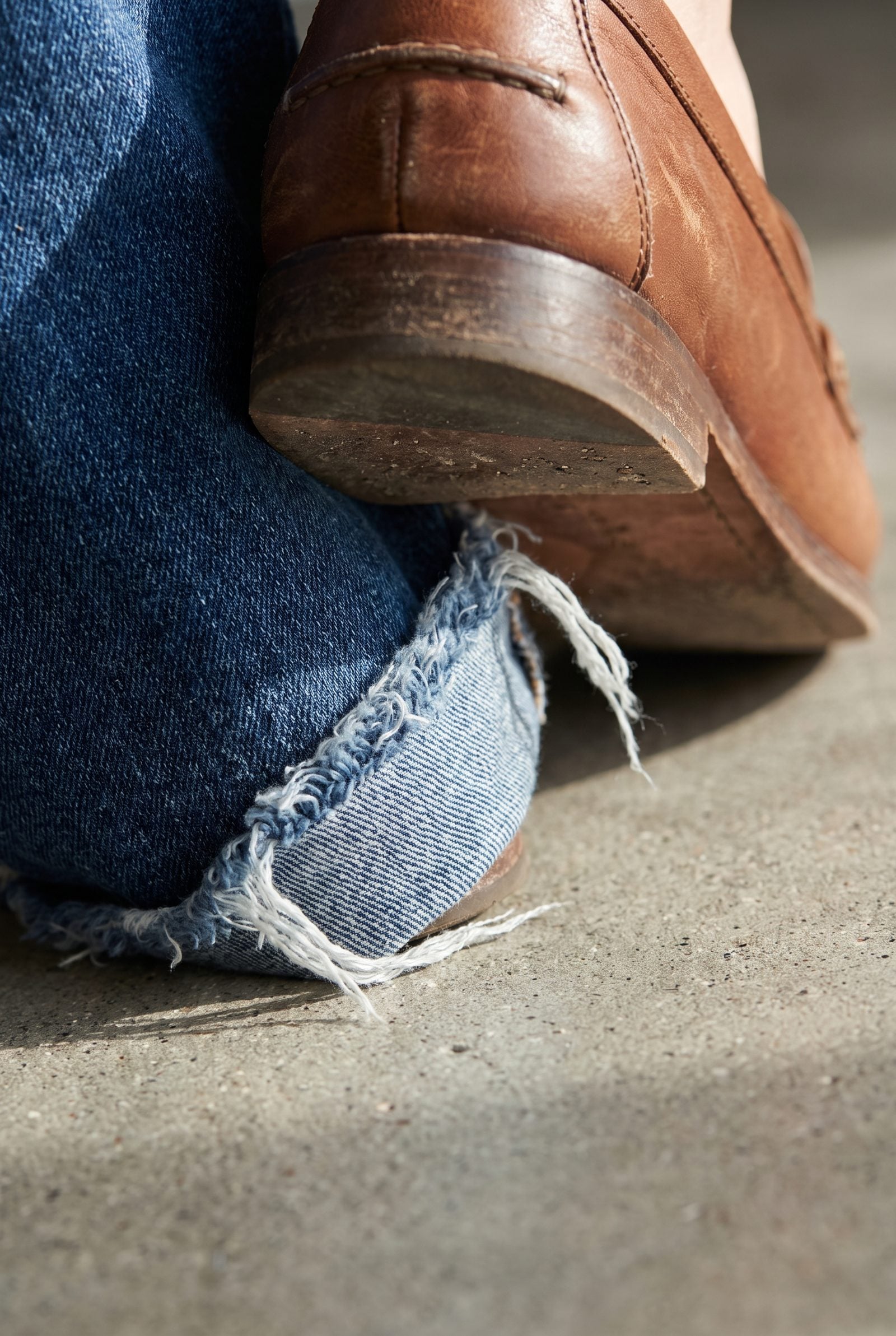 Woman in raw-hem indigo jeans and black loafers, the frayed hem folding under the loafer heel.