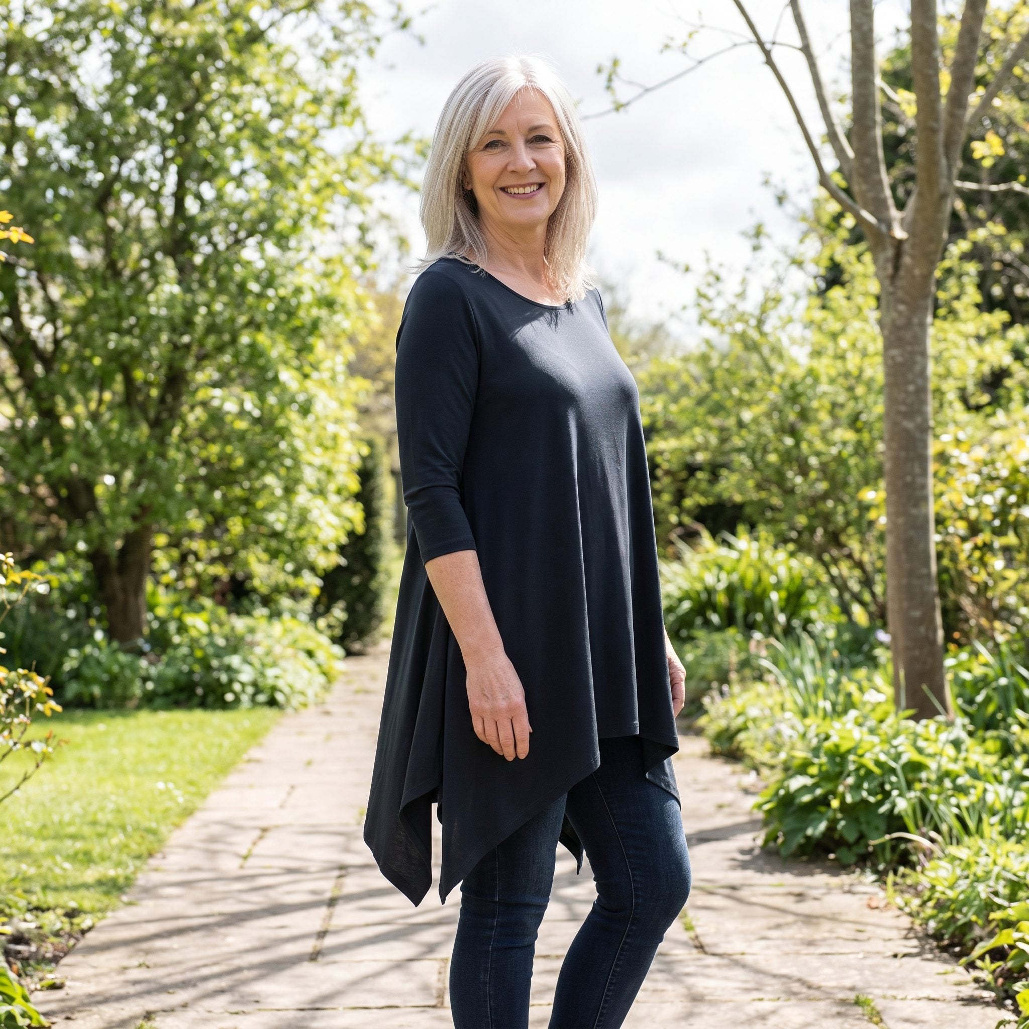 Woman in dark skinny jeans and a loose patterned top with pointed sharkbite hems hanging unevenly down both sides