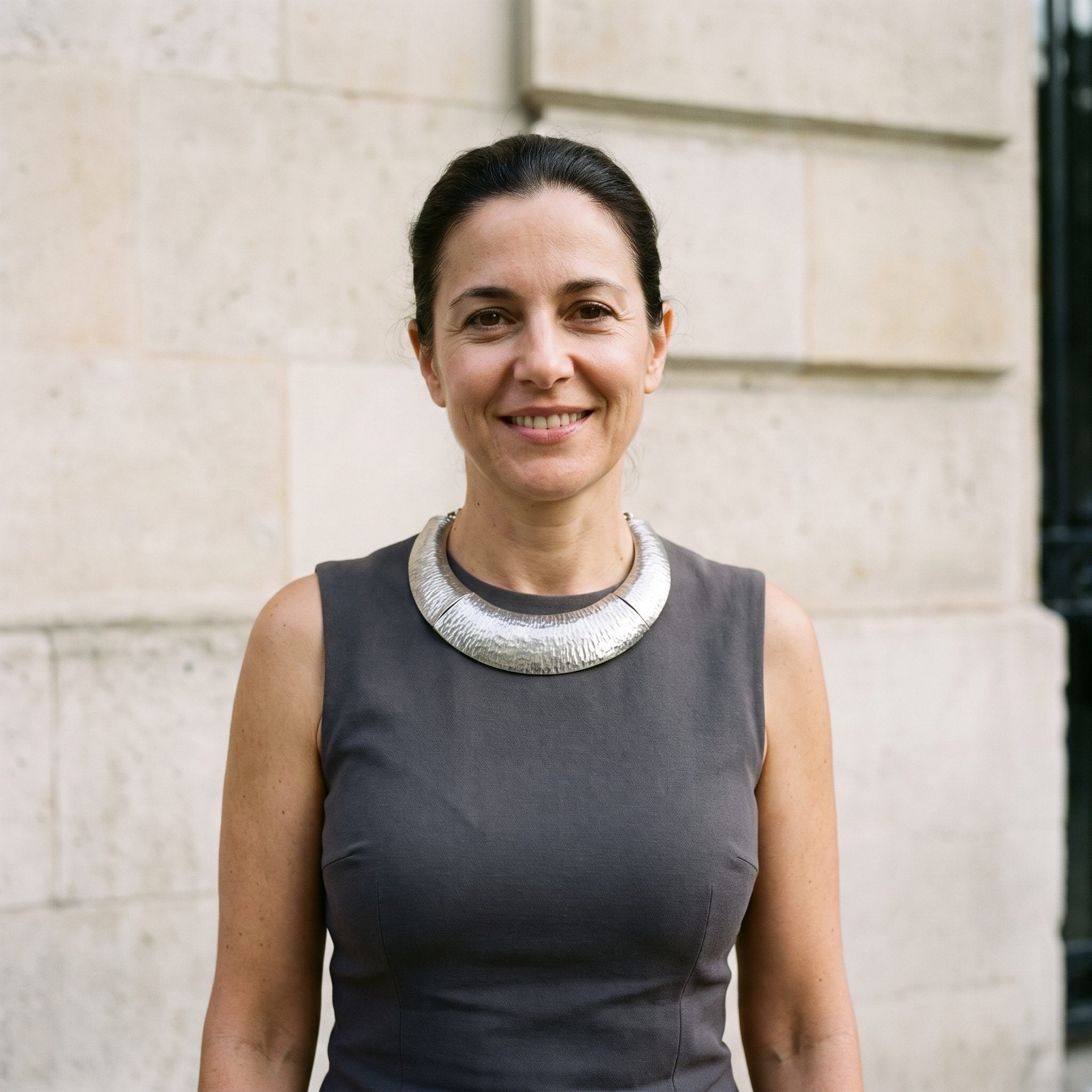 Petite woman in a charcoal sleeveless top with a very wide rigid necklace spanning shoulder to shoulder.