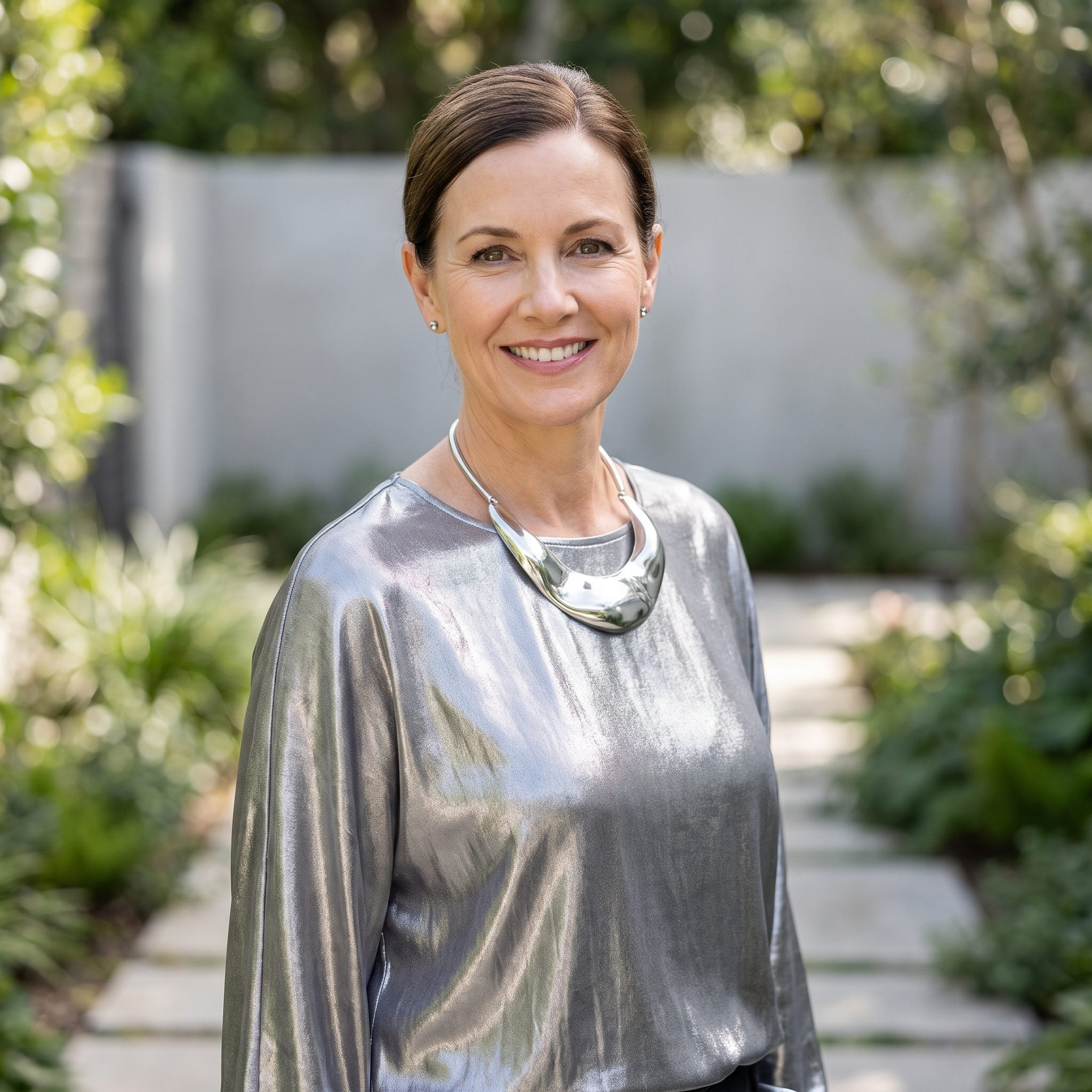 Woman in a metallic silver blouse with a polished silver necklace that blends into the fabric's shine.