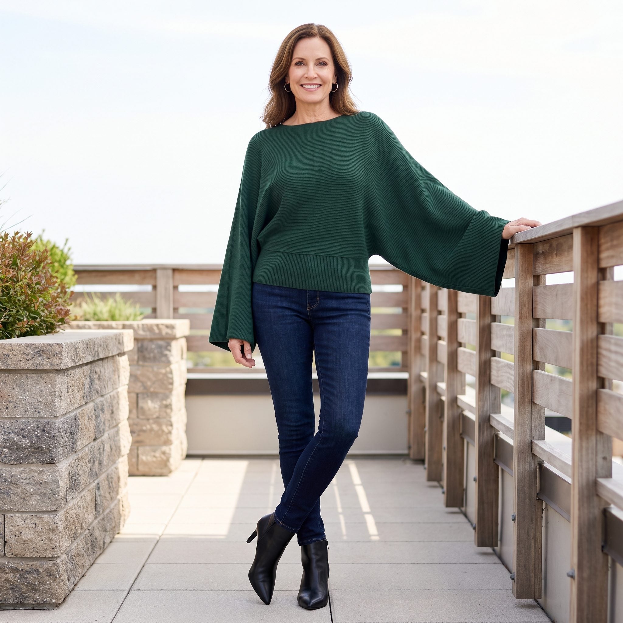 Woman in deep-indigo skinny jeans and an oversized deep-green dolman-sleeve batwing sweater.