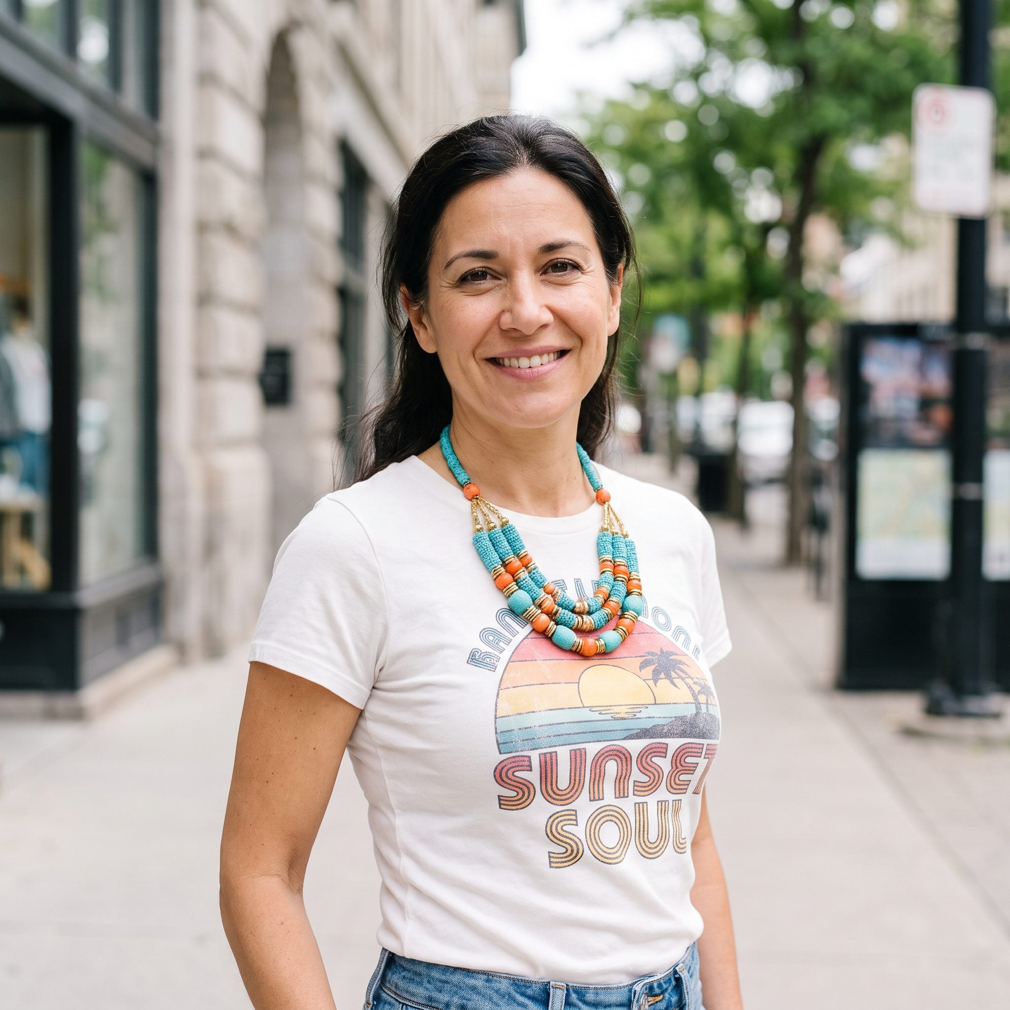 Woman in a white graphic T-shirt with a colorful print wearing a multicolored statement necklace over the artwork.