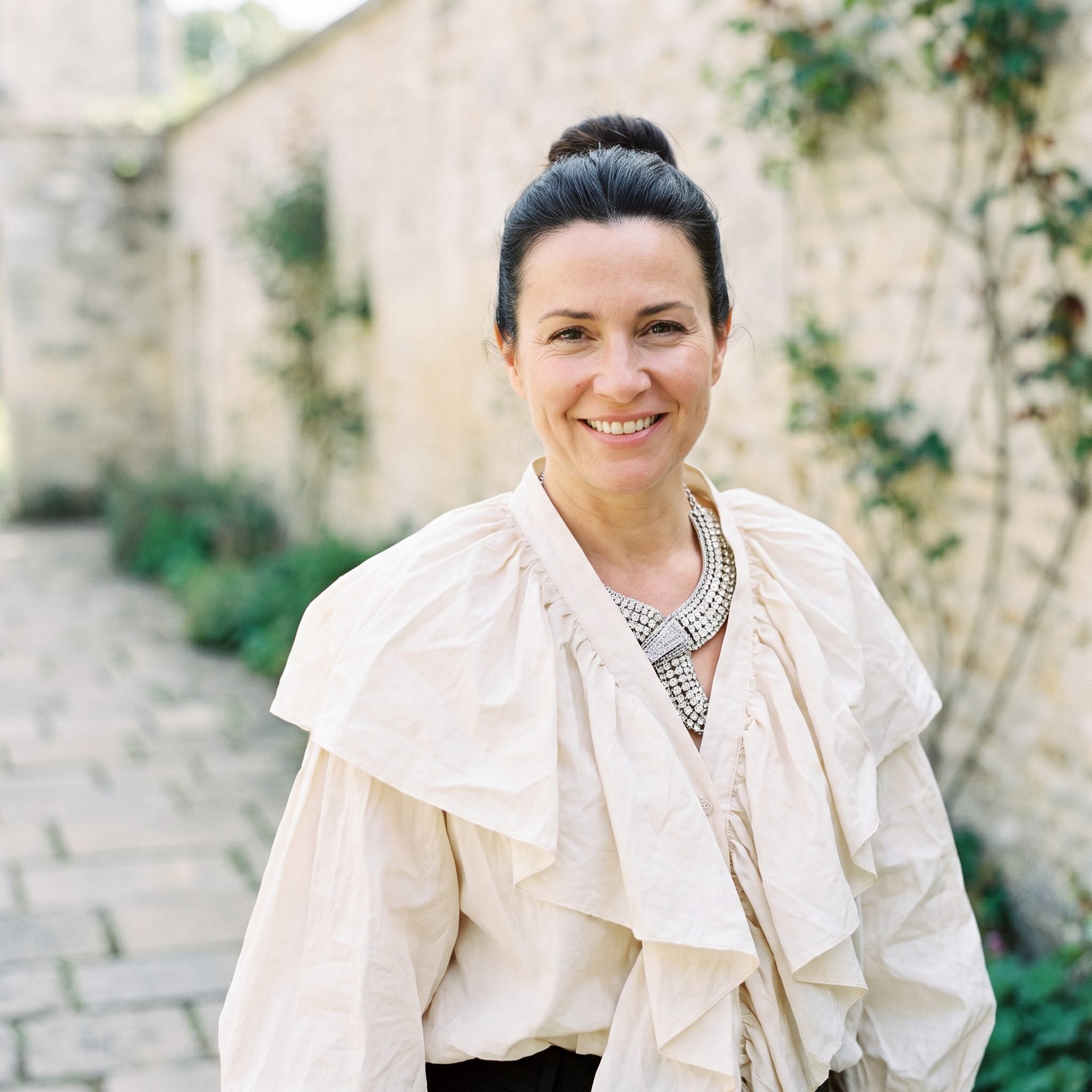 Woman in a ruffled ivory blouse with a structured necklace unable to sit flat among the fabric folds.
