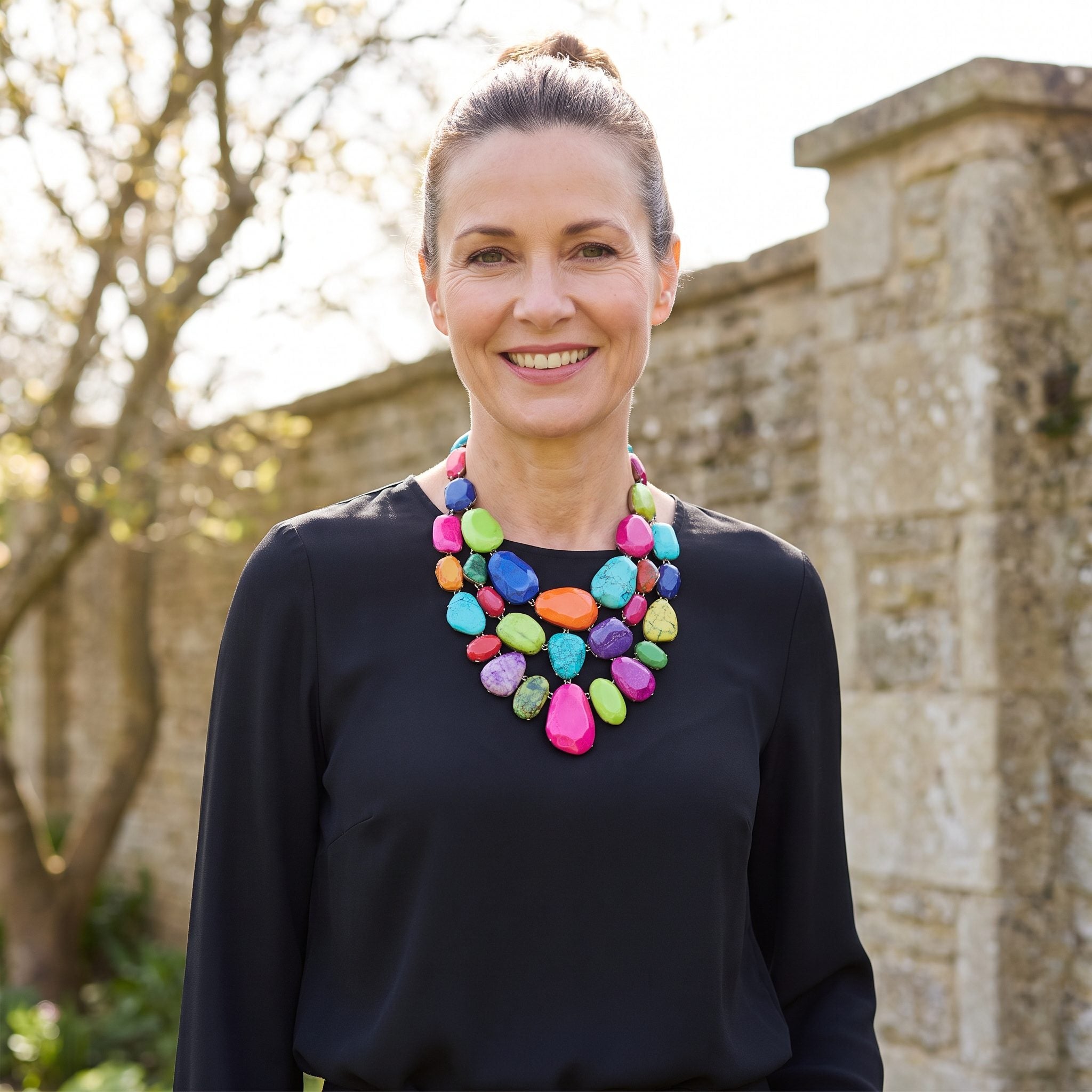 Woman in a plain black blouse wearing a single large necklace crowded with eight unrelated saturated colors and stone shapes.