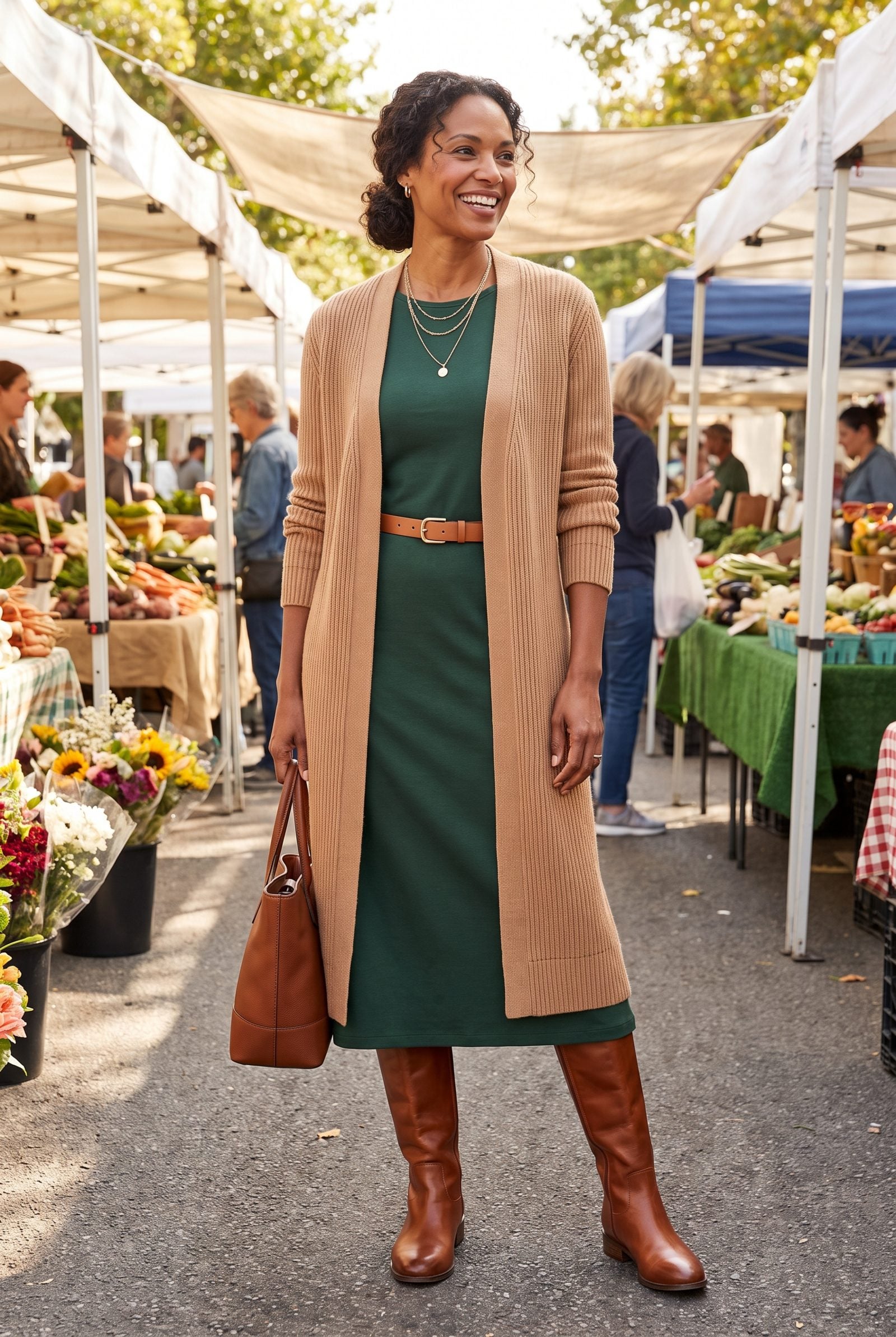 Woman in a long camel cardigan and green midi dress ending at the same mid-calf height, with cognac riding boots.
