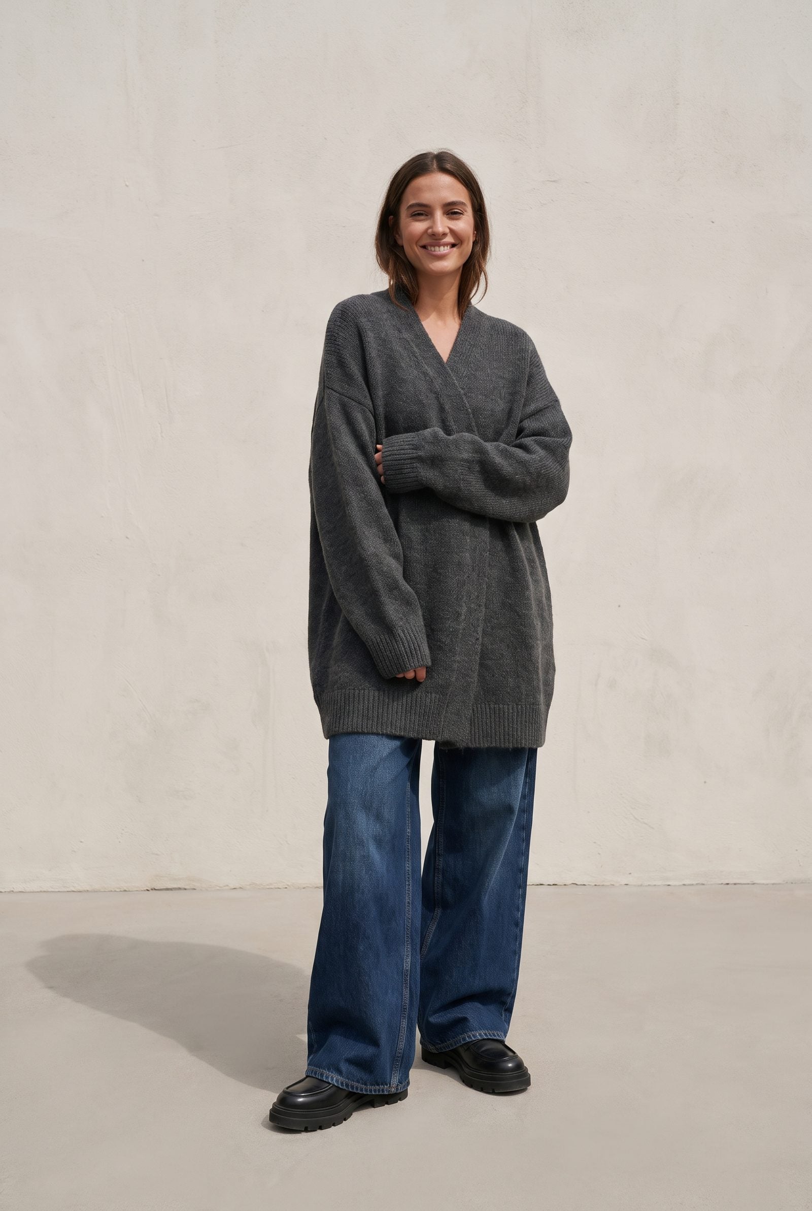 Woman in wide light-wash jeans, chunky loafers, and a long shapeless taupe cardigan on a park path.