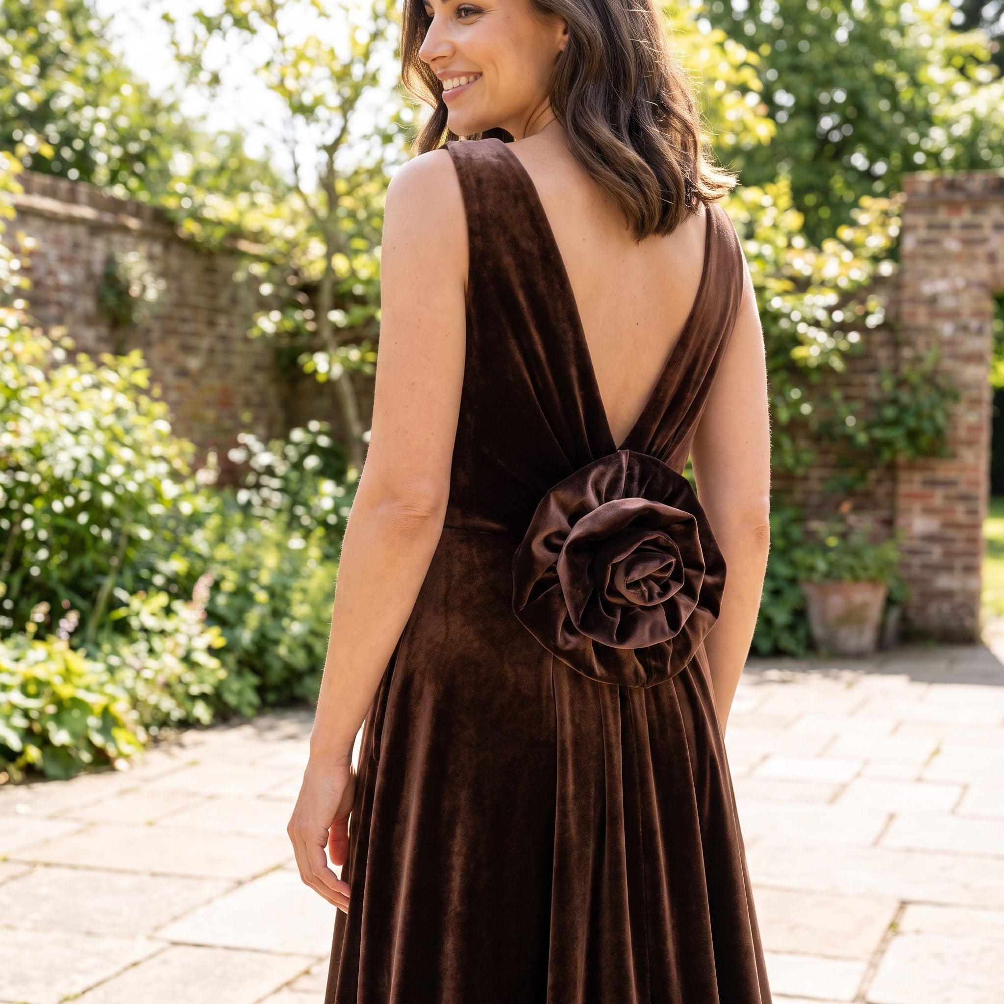 Chocolate velvet evening gown with a deep V back and sculptural rosette detail