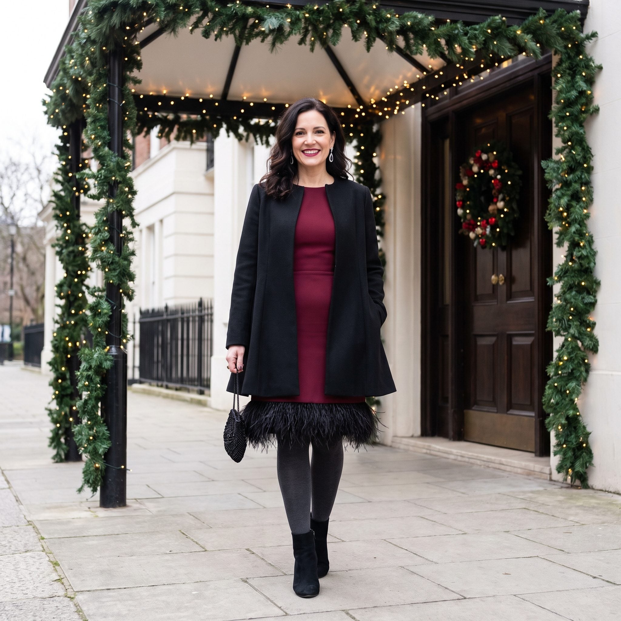 Black wool coat ending above the feather-trimmed hem of a burgundy cocktail dress