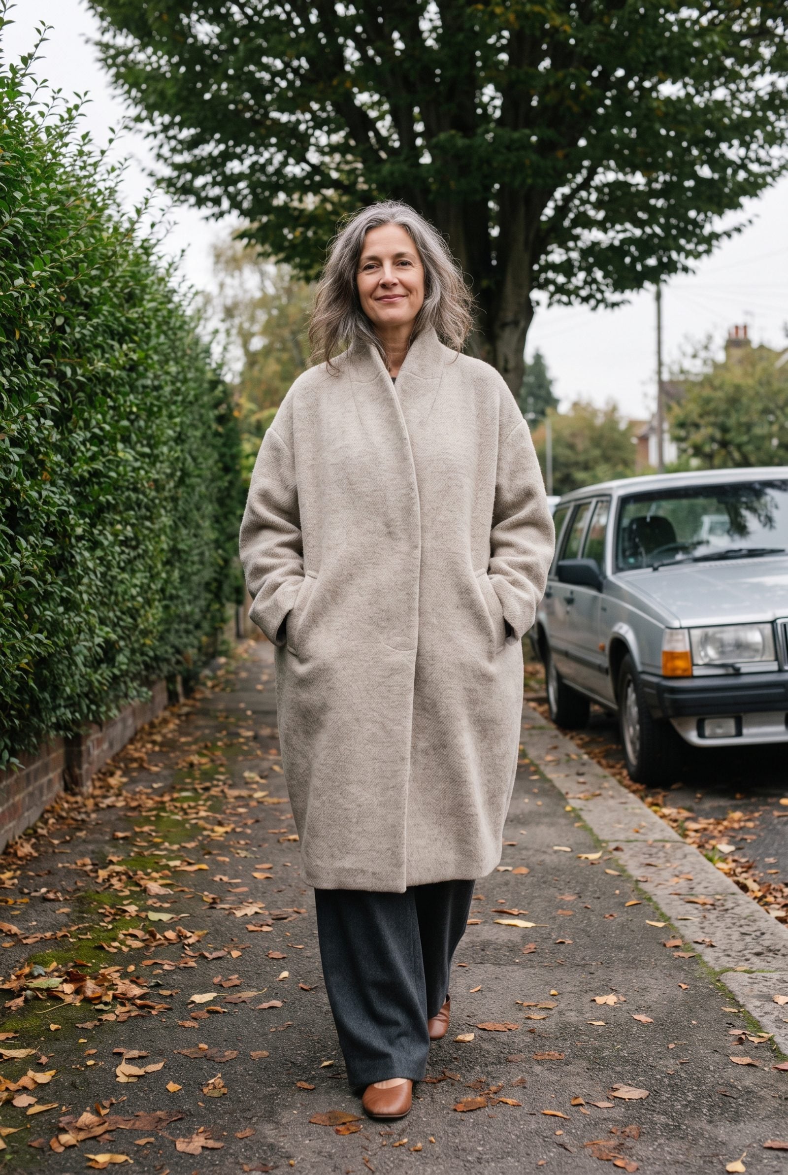 Woman in an oversized oatmeal cocoon coat walking on a residential sidewalk.