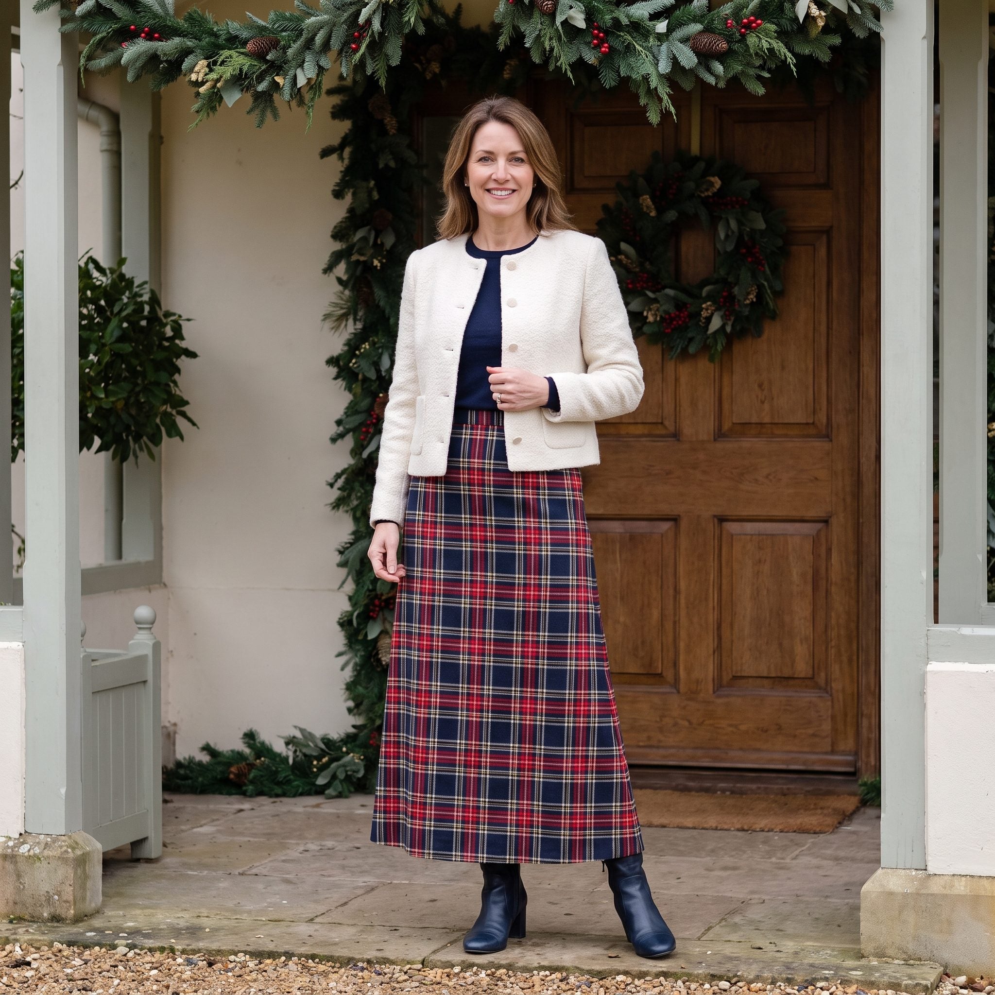 Woman in a cream bouclé jacket and red-navy tartan maxi skirt beneath a decorated porch