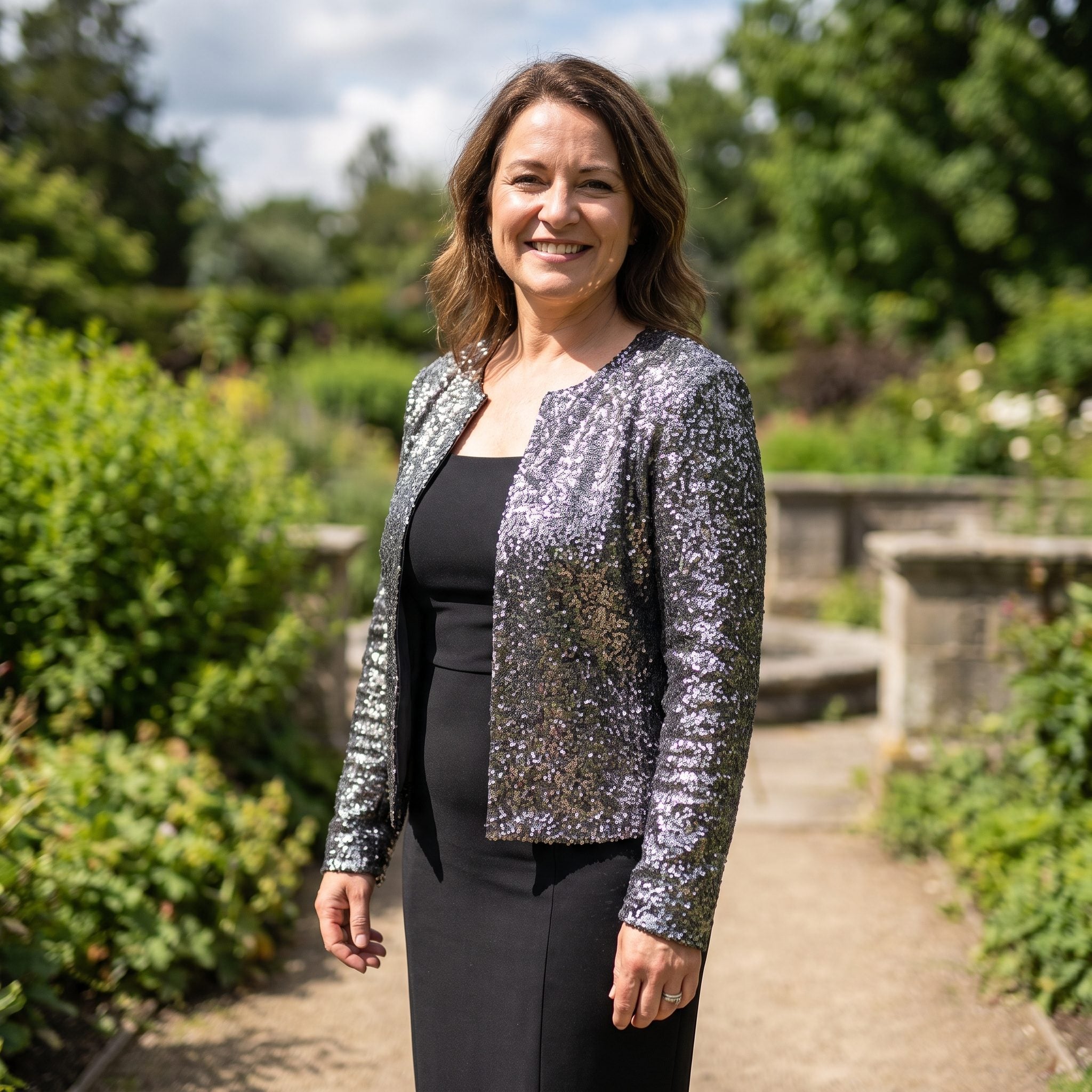 Pewter sequined cropped evening jacket worn over a long black column dress