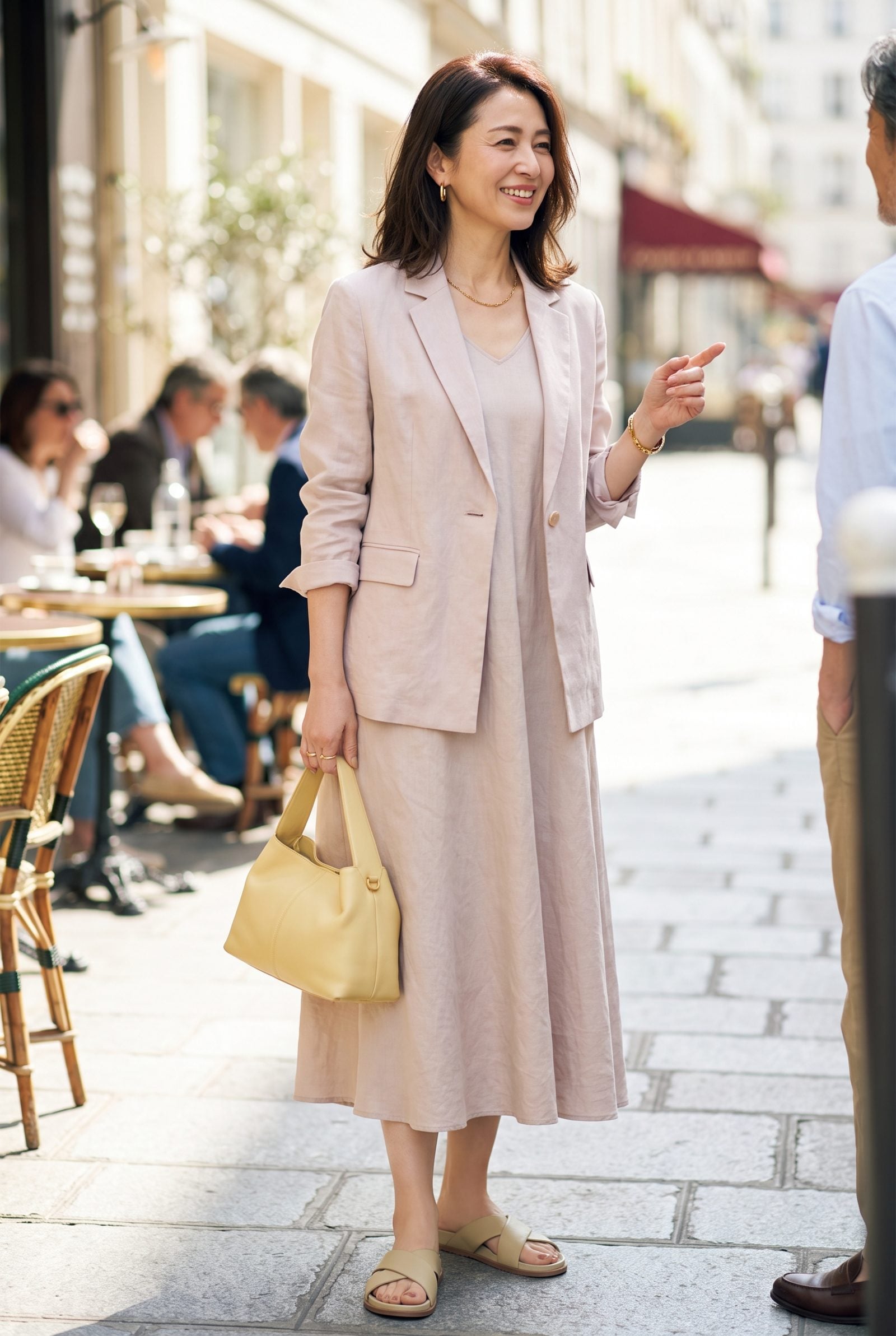 Woman in a garden holding a dusty-pink structured leather top-handle bag with both hands.