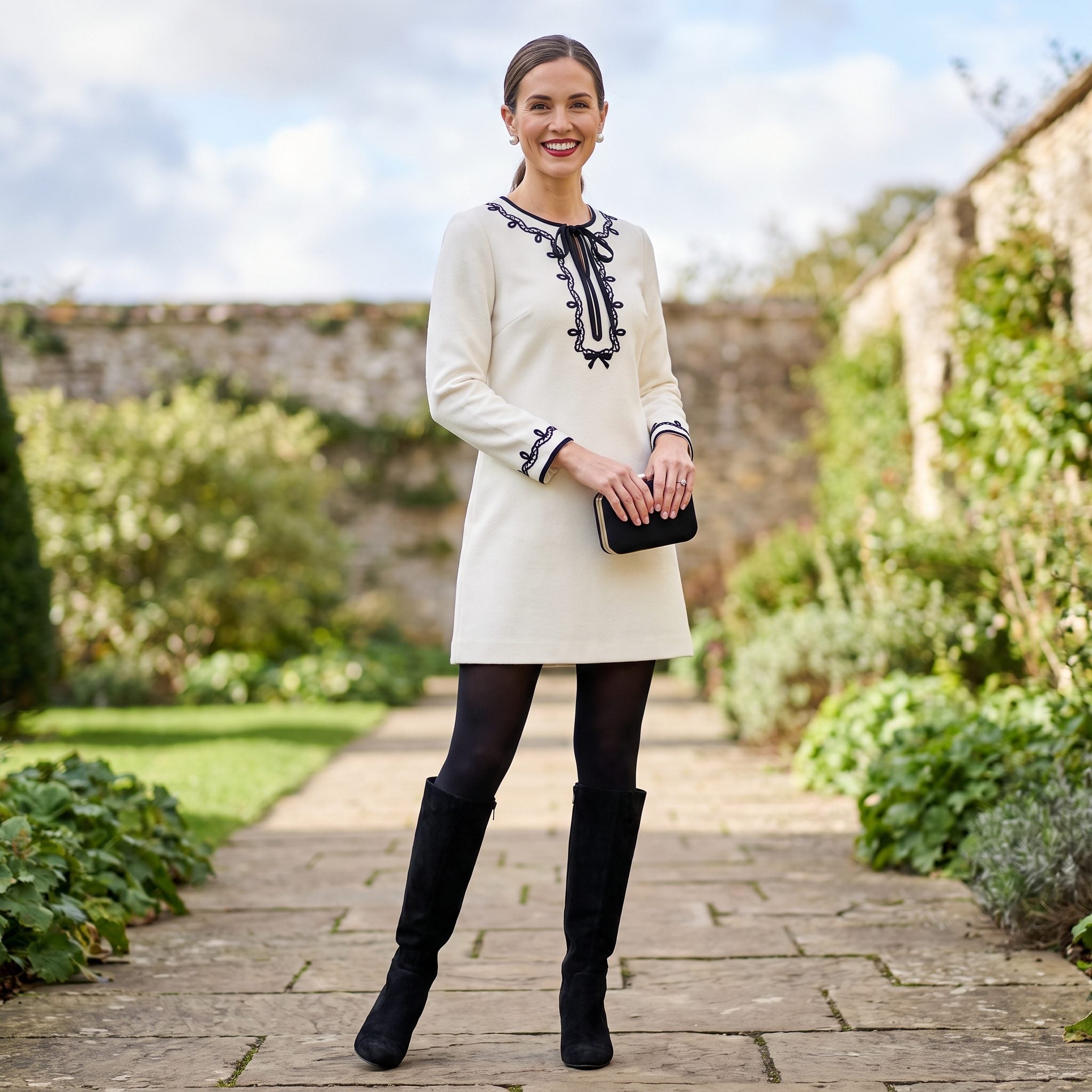 Winter-white wool dress with black ribbon embroidery, tights, and tall boots